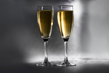 Two glasses with golden champagne on a sparkling metal background.