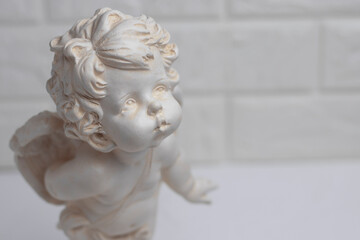 White plaster figurine of an angel on a brick wall background. Decorations in the interior.