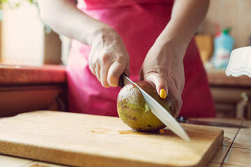 Female hands with a knife cut a mango on a cutting board.