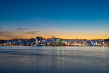 St. John's, waterfront harbour at night during the blue hour. The lights on the water are bright yellow and orange which are reflecting from the skyline in the stillness of the smooth water.  