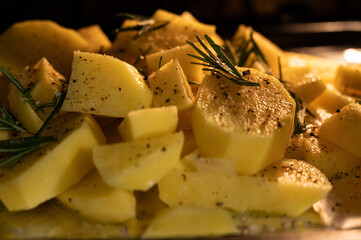 Close up shot of a pan inside the oven full of potatoes with salt, pepper and rosemary, the yellow light of the oven envelops them.