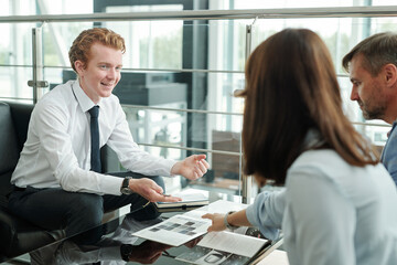 Fototapeta premium Happy young manager sitting in front of couple and looking at female client