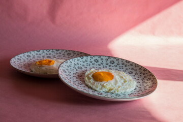 Homemade meal, Organic tasty cooked eggs for healthy breakfast on pink background, fancy ceramic plates, and flowers in a vintage artistic composition. Simple food composition