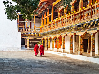 Two Buddhist monks in their traditional red dress walking in the monastery Punakha Dzong courtyard, Bhutan.