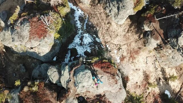 A top down capture of a couple standing at the top of rock formation hiding between tall forest in Austrian Alps. Early spring in Alps. The nature wakes up after hibernation. Adventure and achievement