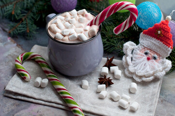 Cup of hot cocoa with marshmallows, santa claus and santa staff. Cup of New Year's and Christmas cocoa with marshmallows with fir branch and sweets on grey background. Top view