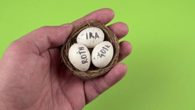 Conceptual composition. Pension savings. The man holds in his hand three eggs with the inscriptions IRA, 401k, Roth which lie in the nest. Close-up
