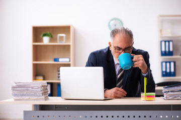 Old businessman drinking coffee at workplace
