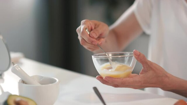 Close-up of adding some cream from jug to bowl with whisked egg mixing all together to make nourishing face mask