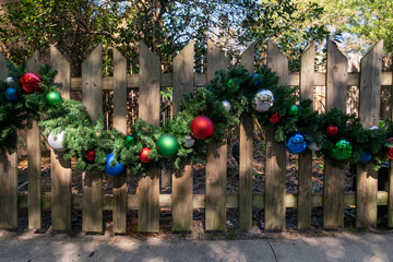 A light coloured textured wooden paling fence with a Christmas garland looped along the middle of...