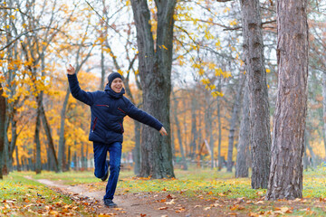 a boy running through the park and enjoys autumn, beautiful nature with yellow leaves