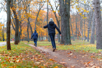 teen girl and boy running through the park and enjoys autumn, beautiful nature with yellow leaves