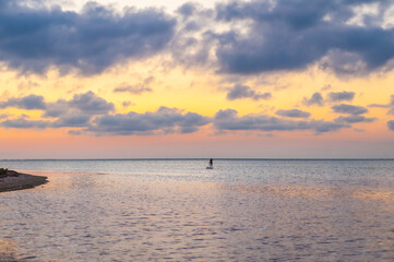 A girl silhouette on a stand up puddleboard on stunning colorful sea sunset background