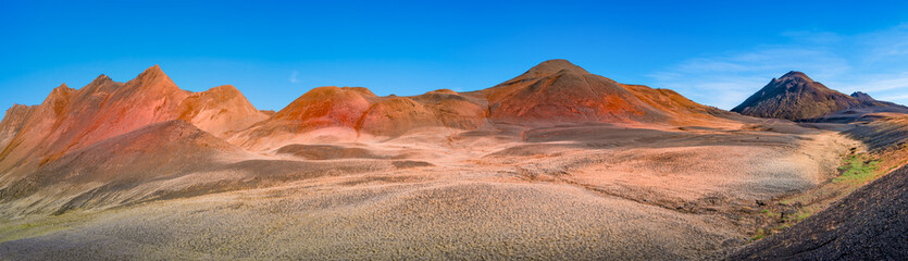 Panoramic view over volcanically active zone in Highlands of Iceland, resembling Martian red planet landscape, with black volcano and red slopes, at summer and blue sky.