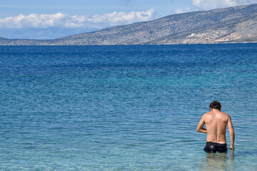 A handsome man enters the sea. A man goes swimming. Sunny day on the beach, blue sky above the blue sea.