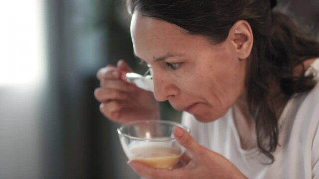 Close up of good-looking middle-aged woman having beauty ritual applying rejuvenating egg mask on face with brush looking at mirror in living room