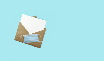 White sheet in craft brown mail envelope and medical face mask on light blue background. Christmas wish list and gifts during lockdown. top view. Copy space