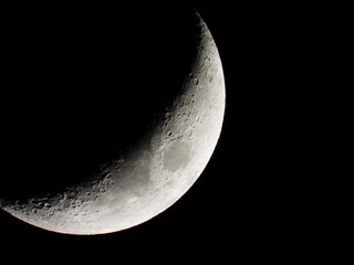 Naklejka premium Young growing moon close up against the black sky