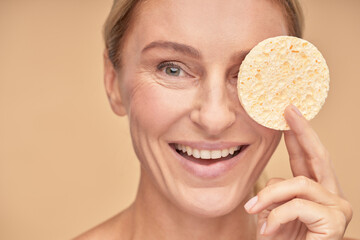 Happy mature lady holding sponge near her face