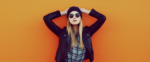 Portrait of stylish young blonde woman model in black rock style over a orange background