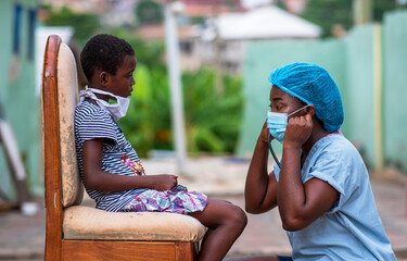 An African nurse putting stethoscope in ear and wearing a face mask for protection in covid-19...
