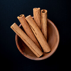 Cinnamon sticks in a bowl on black background.