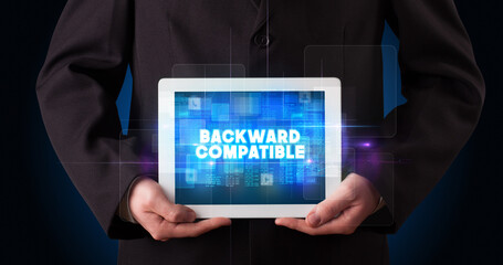 Young business person working on tablet and shows the inscription: BACKWARD COMPATIBLE
