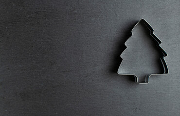 Shape for cookies in the form of a Christmas tree on a dark background on the right side, space for text on the left