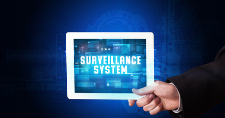 Young business person working on tablet and shows the digital sign: SURVEILLANCE SYSTEM