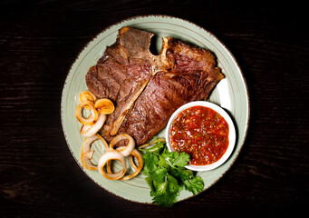 Roasted meat on a plate. Restaurant food. Grilled meat steak with sauce. Wooden background. Top view.