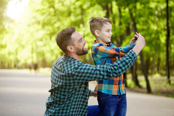 A father teaches his son to take a selfie on his phone in a Park on a Sunny summer day. Father's...