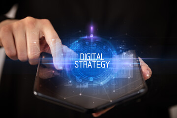 Young man holding a foldable smartphone with DIGITAL STRATEGY inscription, educational concept