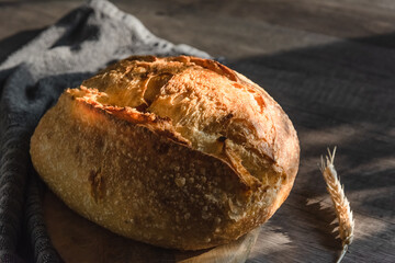 The handcrafted tartin bread lies on a wooden surface next to wheat ears. Farming and home baking concept
