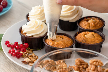 Closeup view of female baker hand decorating tasty cupcake with whipped cream top