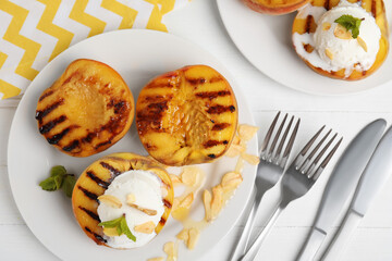 Delicious grilled peaches with ice cream served on white wooden table, flat lay
