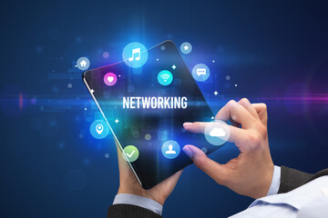 Fototapeta premium Businessman holding a foldable smartphone with NETWORKING inscription, social media concept
