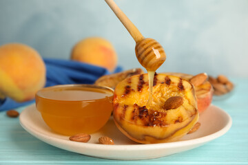 Pouring honey onto delicious grilled peach on light blue wooden table, closeup