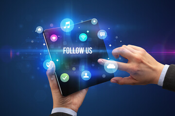 Businessman holding a foldable smartphone with FOLLOW US inscription, social media concept