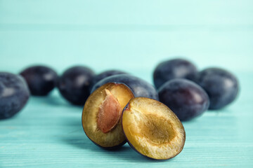 Fototapeta premium Delicious ripe plums on light blue wooden table, closeup. Space for text