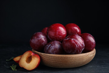 Fototapeta na wymiar Delicious ripe plums in wooden bowl on black table