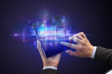 Obraz na płótnie Canvas Businessman holding a foldable smartphone with BROADBAND inscription, new technology concept