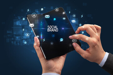 Businessman holding a foldable smartphone with SOCIAL BRAND inscription, social networking concept
