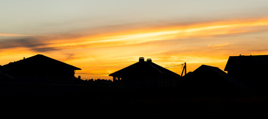 Fototapeta na wymiar House silhouettes against orange sunset sky