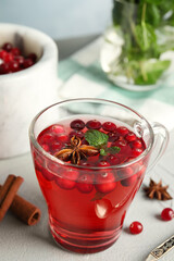 Tasty hot cranberry tea with mint and fresh ingredients on light table