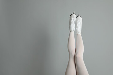 Woman in elegant white ice skates on grey background, closeup of legs. Space for text