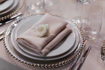 Set of plates with beige napkin above. Luxury table set in the restaurant. Glasses and plates. Decorations. Beige background. Wedding banquet. 
