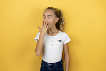 Young beautiful child girl standing over isolated yellow background bored yawning tired covering mouth with hand. Restless and sleepiness.