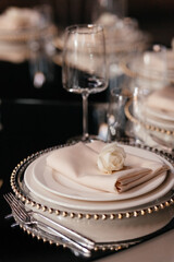 White rose on the set of plates on the dark background. Luxury table set in the restaurant. Glasses and plates. Wedding banquet. 