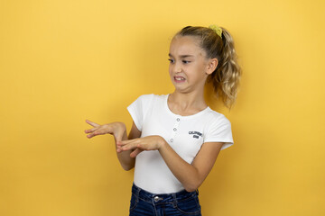 Young beautiful child girl standing over isolated yellow background disgusted expression, displeased and fearful doing disgust face because aversion reaction