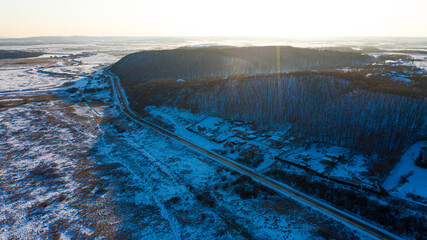 Snow-capped hills and road at sunset background photographed from drone